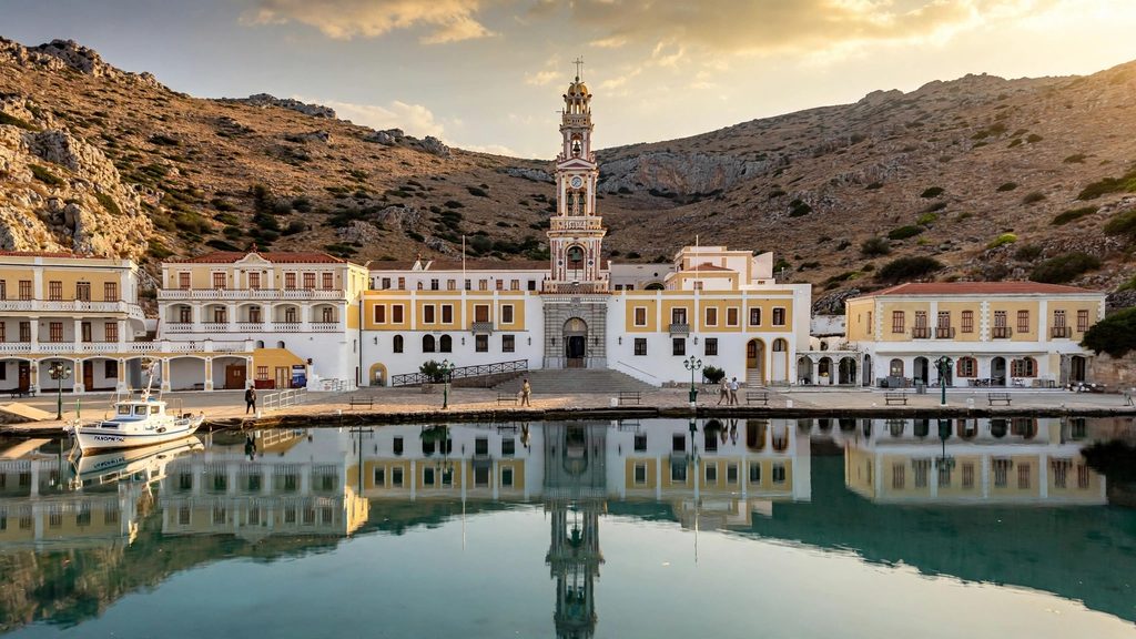 Ornate white bell tower of the Panormitis Monastery above a calm turquoise bay on the south coast of Symi