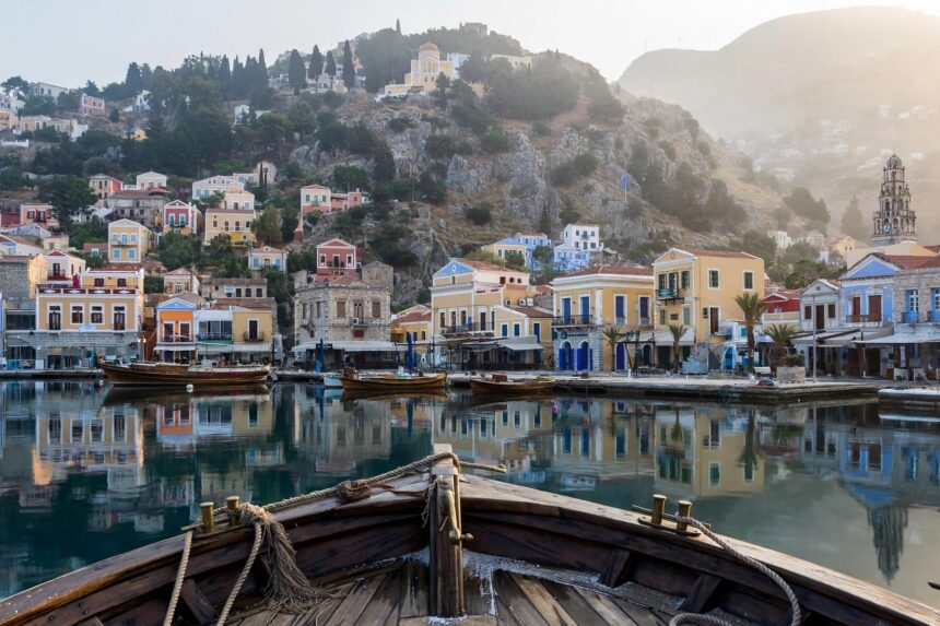 Neoclassical mansions in ochre and pastel colours rising in tiers above the calm harbor of Gialos on Symi at sunrise